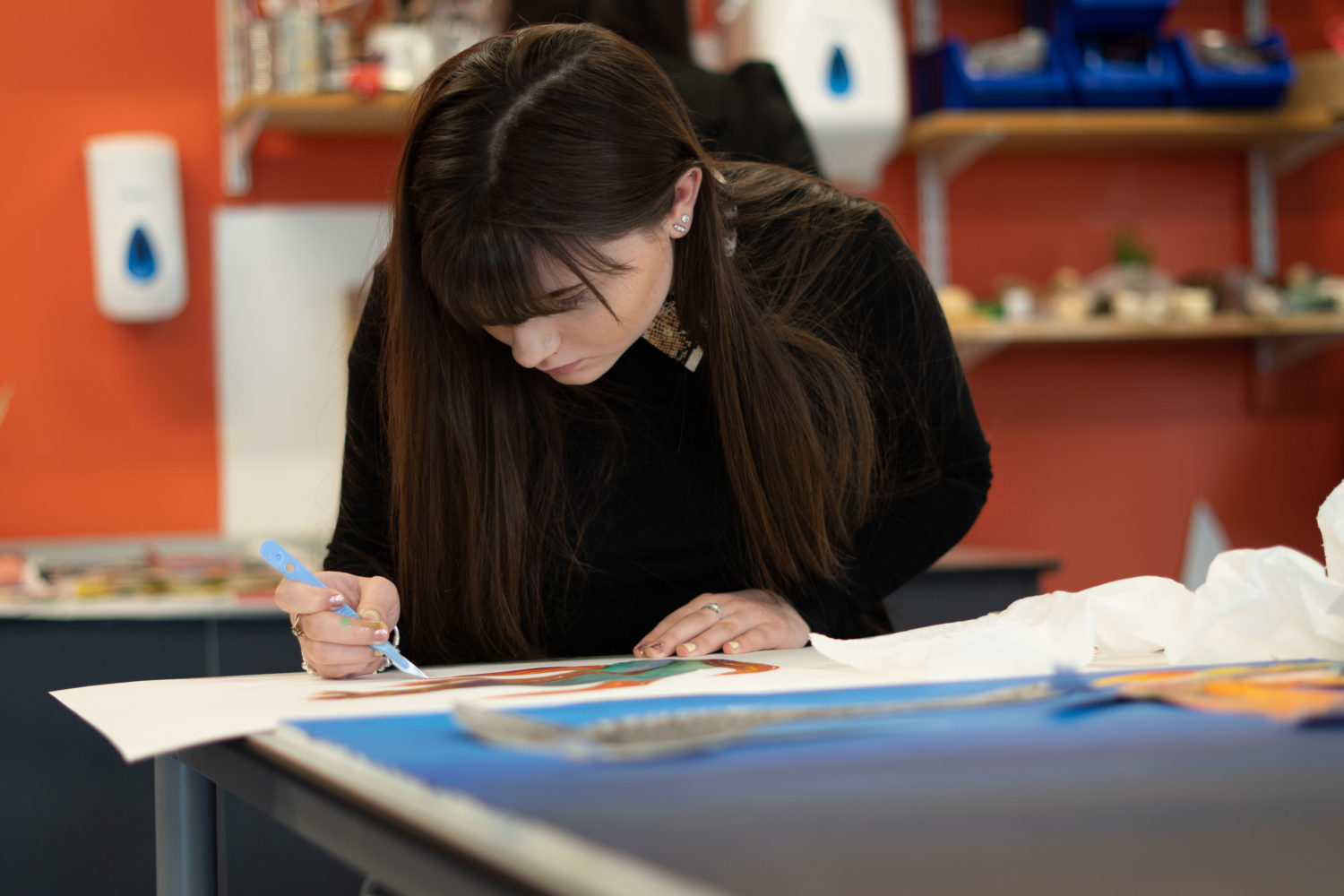An Art student is pictured at The Leigh UTC holding a paint brush whilst sitting at a desk.