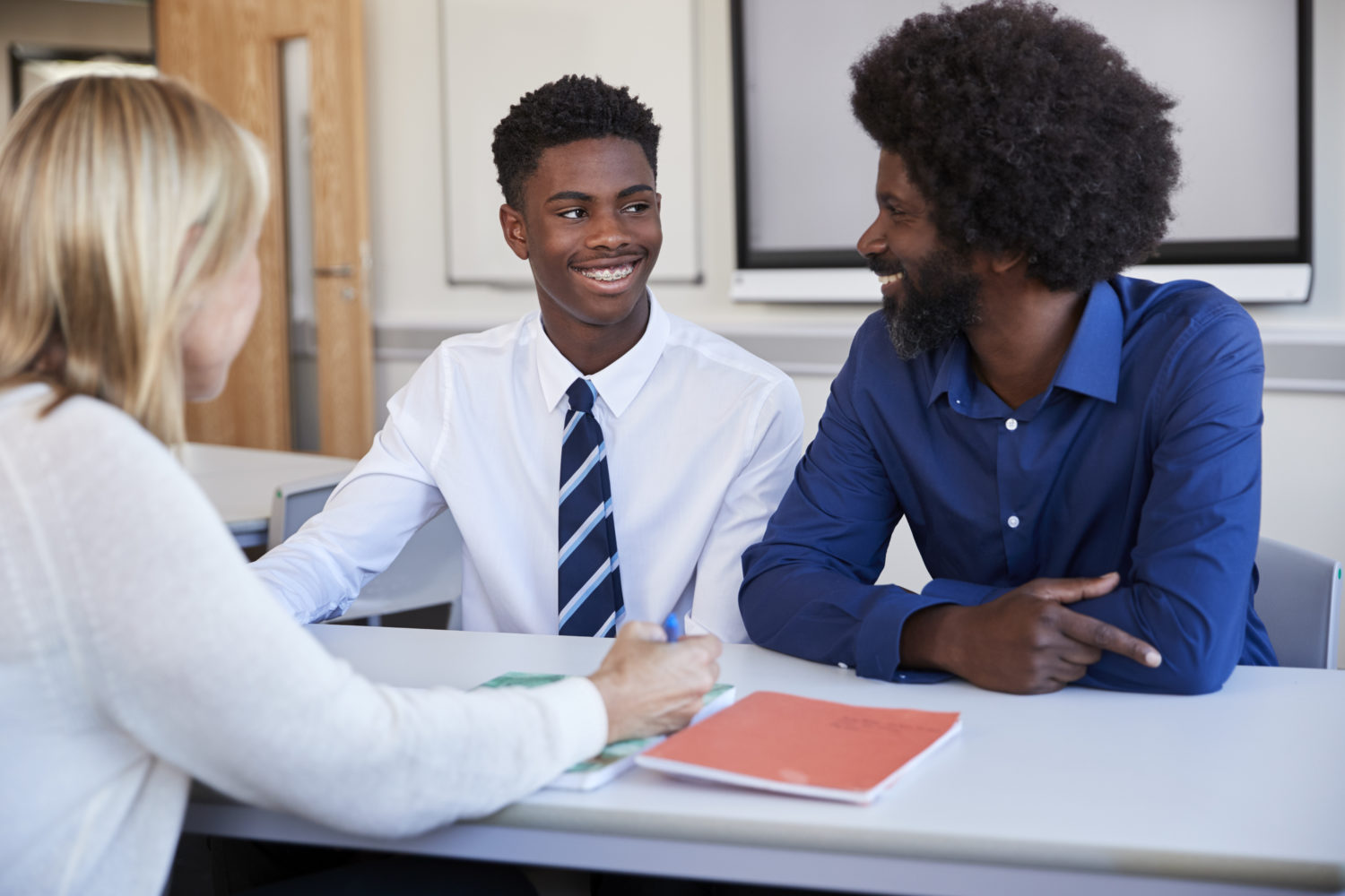 Father And Teenage Son Having Discussion With Female Teacher At High School Parents Evening