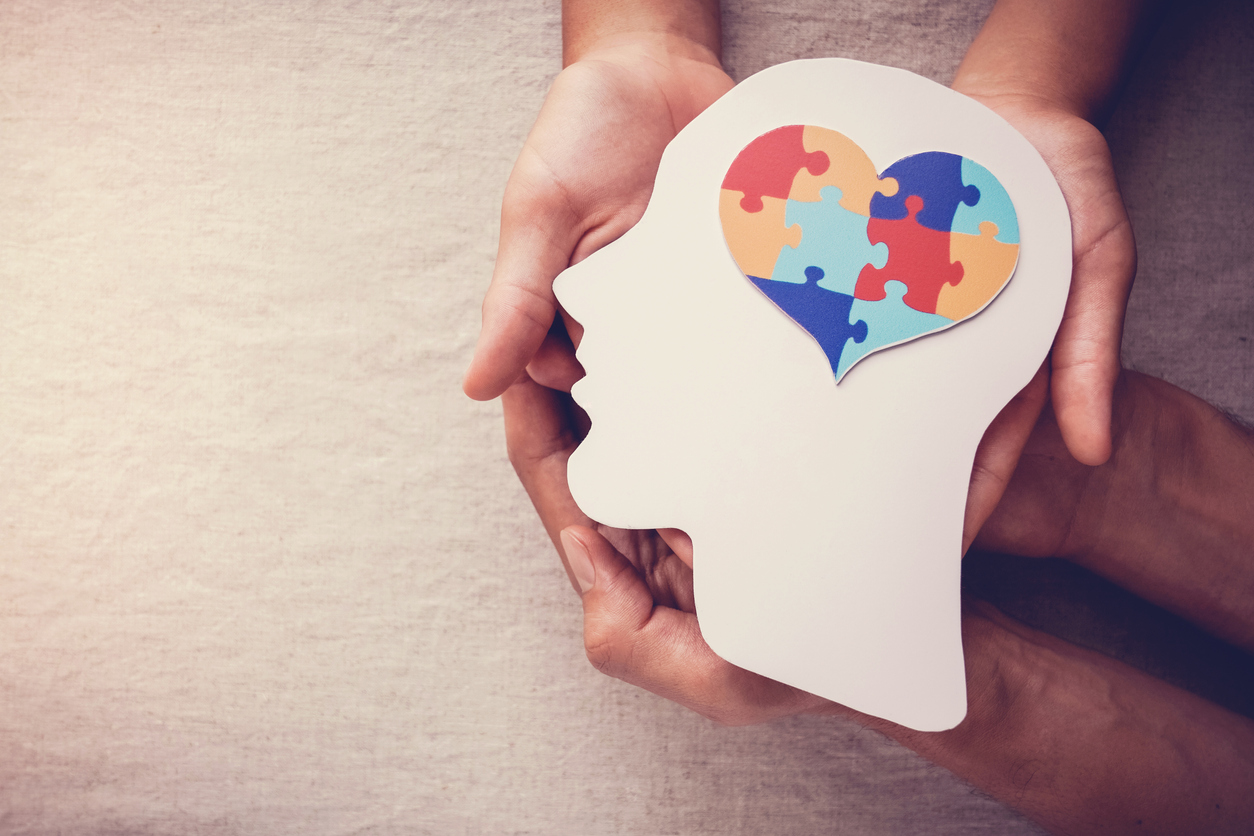 Two people's hands holding a paper cut-out of a head with jigsaw pieces in a heart-shape as the brain