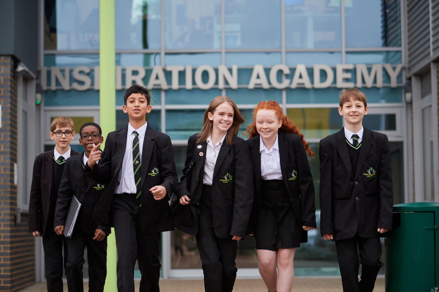 A group of six Inspiration Academy students are seen walking out of the building at the end of the day and towards the camera, with smiles on their faces.